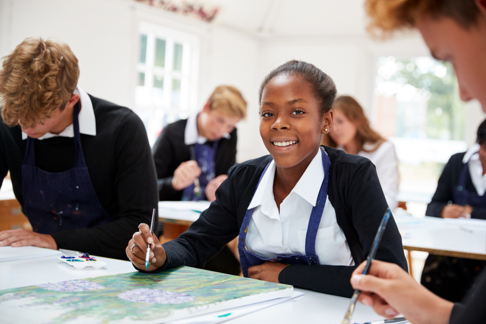 A female student dressed in school uniform sitting in a classroom at a desk with other students in the background